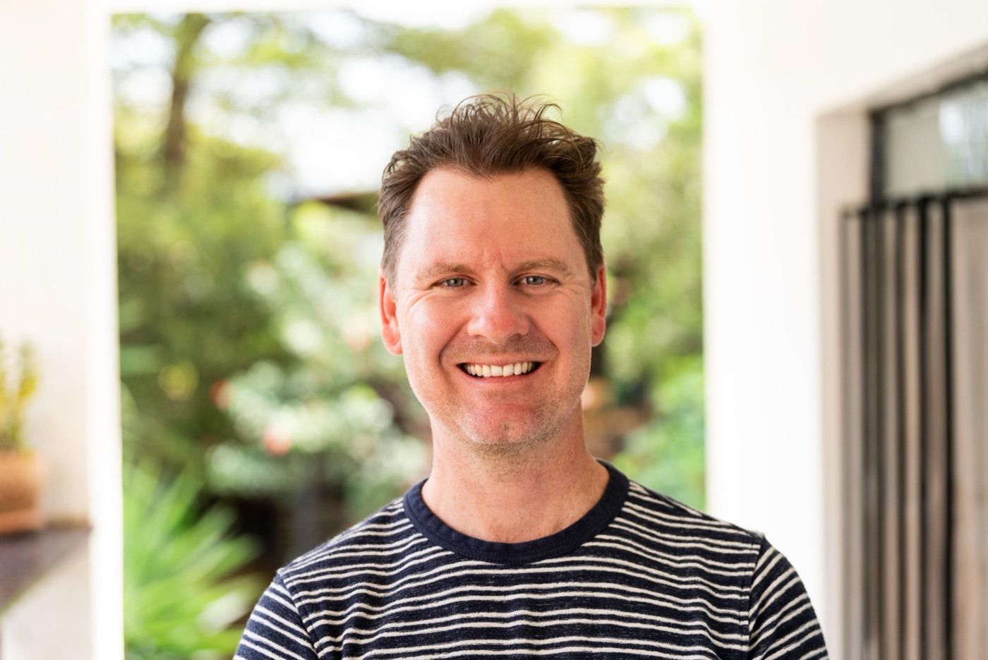 Jeff today, smiling, in a striped T-shirt in front of a garden doorway