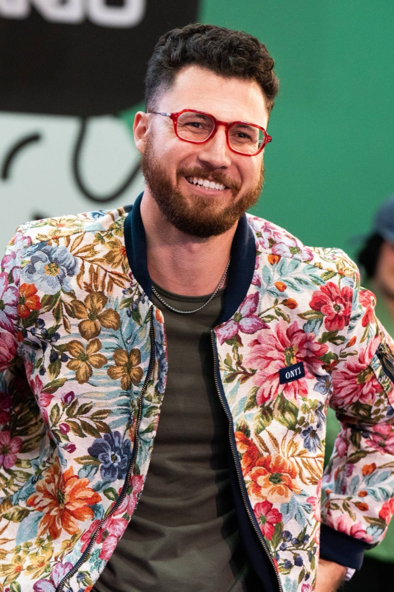 A smiling man in red glasses and a bright floral jacket at a coffee event